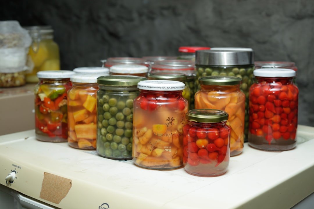 Colorful array of home-fermented vegetables in glass jars including sauerkraut, kimchi, and pickled vegetables on a wooden kitchen counter